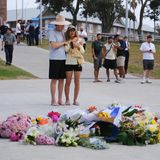 EIn paar steht am Bondi Beach und trauert vor Blumensträußen