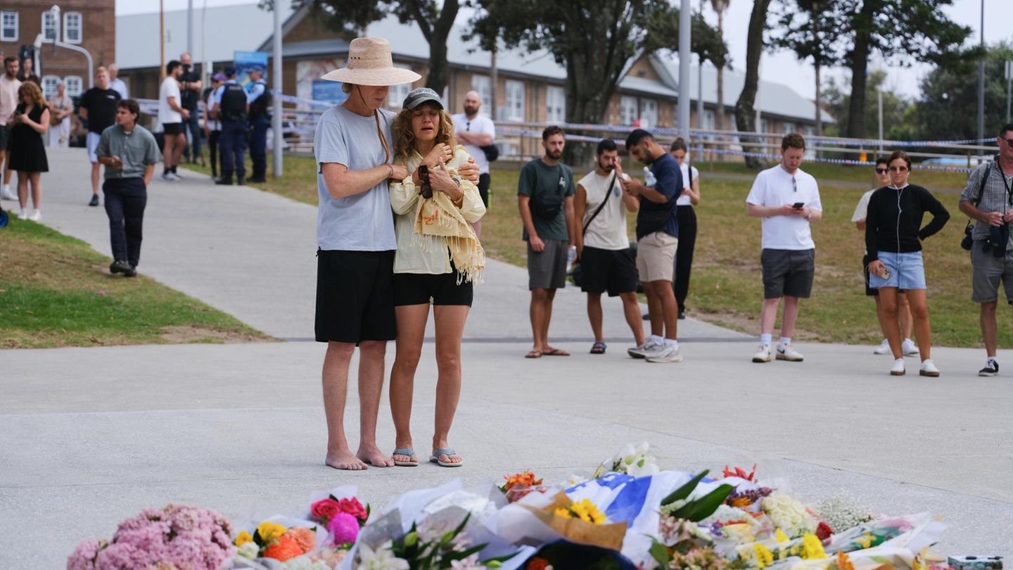 EIn paar steht am Bondi Beach und trauert vor Blumensträußen
