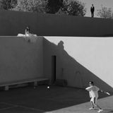 Eine Person spielt Tennis, während im Hintergrund zwei Menschen in Hochzeitskleidung stehen und sitzen