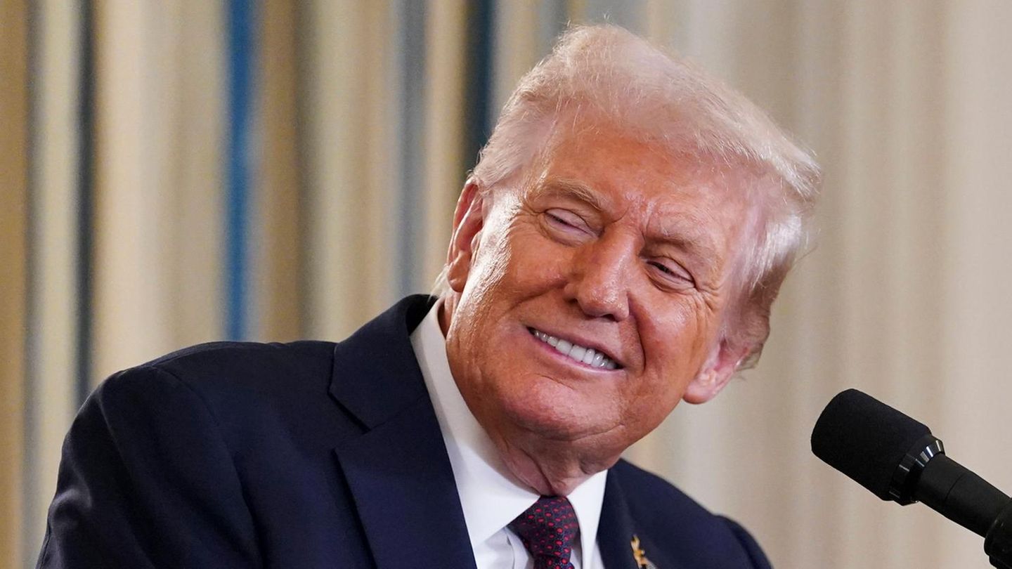 Donald Trump lächelt, während er an einem Rednerpult steht und seinen Kopf nach rechts jemandem zuwendet