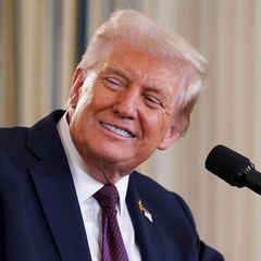 Donald Trump lächelt, während er an einem Rednerpult steht und seinen Kopf nach rechts jemandem zuwendet