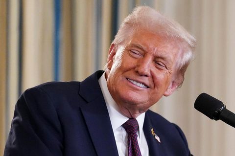 Donald Trump lächelt, während er an einem Rednerpult steht und seinen Kopf nach rechts jemandem zuwendet