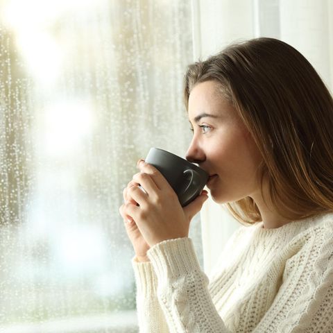 Thema Jahresrückblick: Eine Frau trinkt aus einer Kaffeetasse und blickt nachdenklich aus dem Fenster