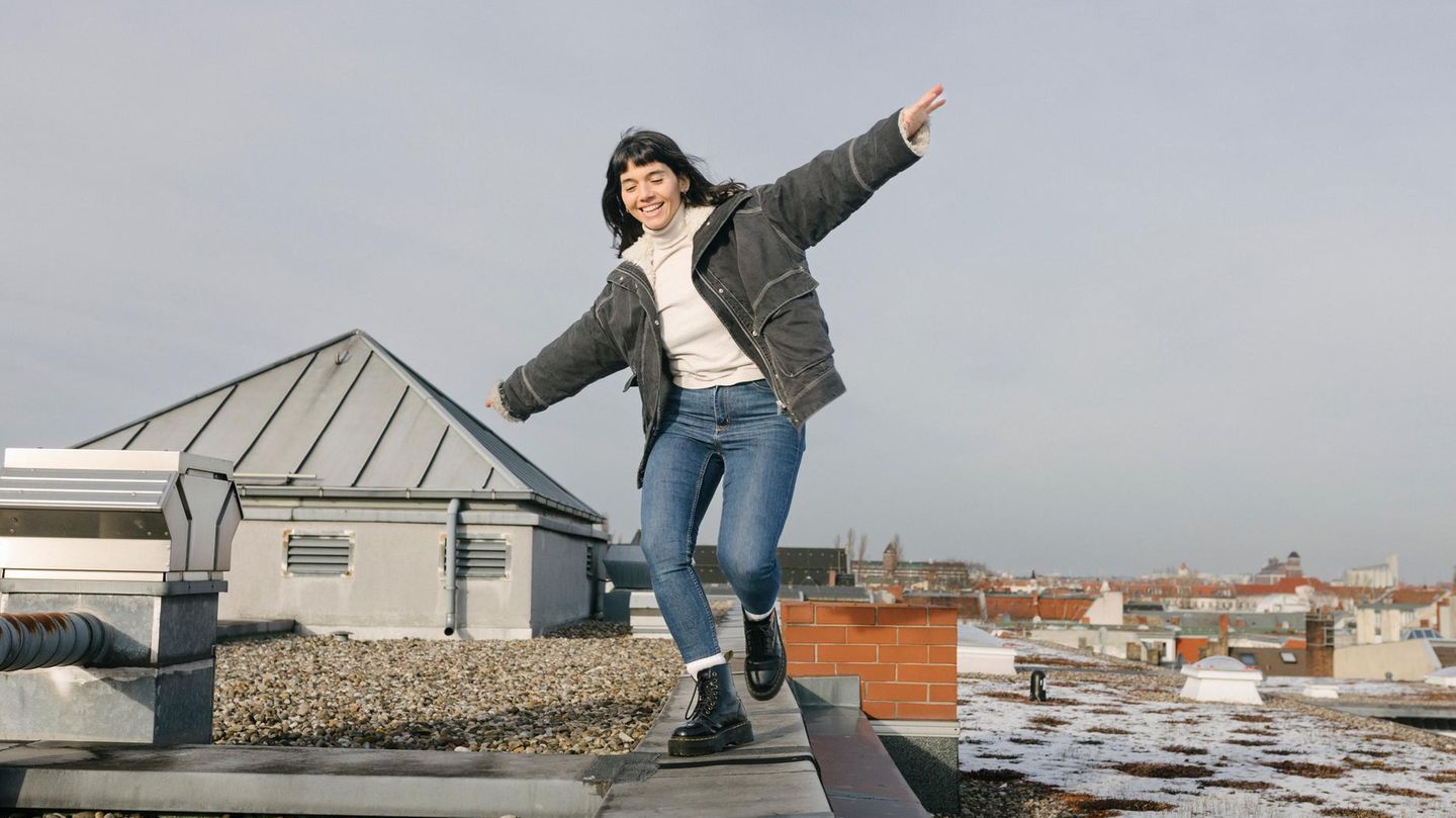 Woman Playfully Balancing On Rooftop With Arms Outstretched -