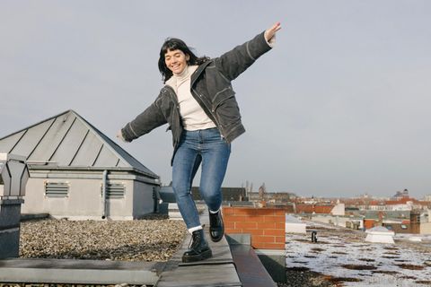 Woman Playfully Balancing On Rooftop With Arms Outstretched -
