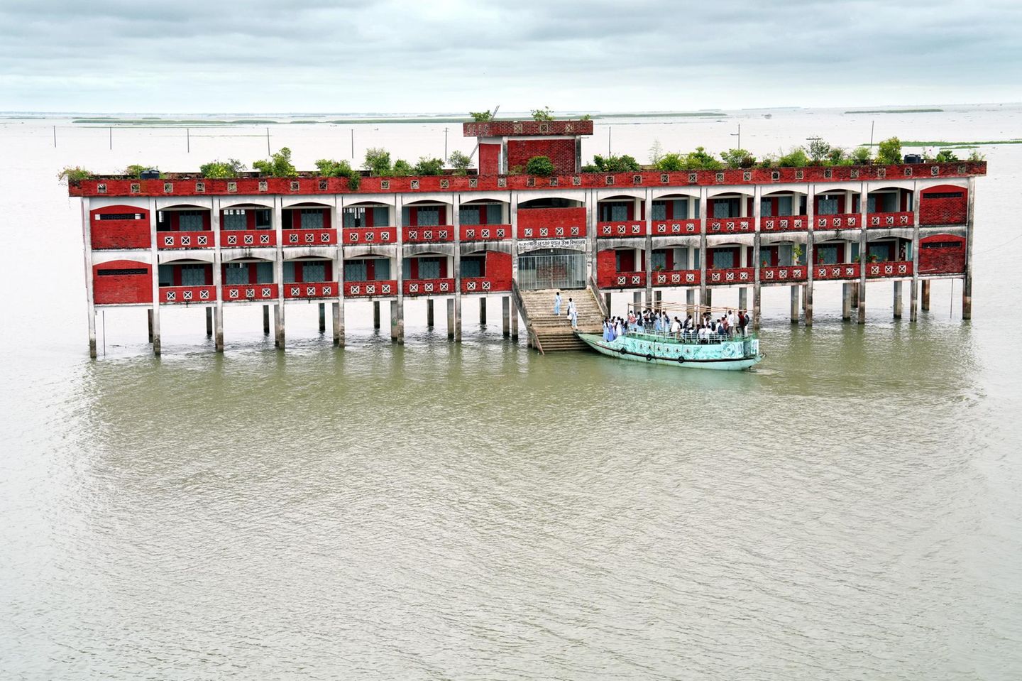 In den Haor-Feuchtgebieten von Kishoreganj, Bangladesch: Fast neun Monate im Jahr ist die Baherbali SESDP Model High School von Hochwasser umgeben und nur mit dem Boot erreichbar. Jeden Tag begeben sich 220 Schüler und zehn Lehrer aus sieben umliegenden Dörfern auf die Reise durch die überflutete Landschaft. Die auf Stelzen erbaute Schule gewährleistet, dass die Kinder trotz schwieriger Umweltbedingungen weiter lernen können