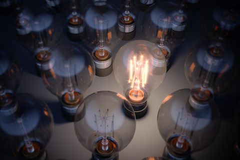 Stromkosten: Eine leuchtende Glühbirne unter vielen dunklen Glühbirnen