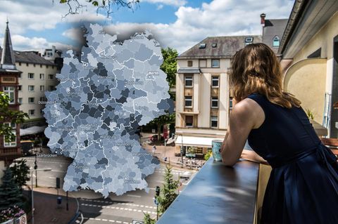 Frau schaut vom Balkon auf eine städtische Straßenkreuzung / über der Kreuzung ist eine Deutschlandkarte ins Bild montiert