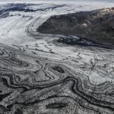Wenn sich Gletscherströme ihren Weg durch das Gebirge bahnen, verschlägt ihre schiere Kraft den Betrachtenden meist den Atem. Die schwarze Vulkanasche, die das Eis des Skeidararjökull hier marmoriert, zeugt jedoch von einem noch gewaltigeren Naturspektakel: dem Wechselspiel zwischen Schnee und Feuer, Sonne und Wind. "Die Vulkaneruptionen liefern die schwarze Asche, welche die Gletscher überdeckt. Darauf fällt frischer Schnee, der allmählich zu Eis komprimiert wird. So legt sich weiße auf schwarze Schicht, viele Male", beschreibt die Geologin Angelika Jung-Hüttl das Phänomen. Je weiter sich der Gletscher seinen Weg ins Tal bahnt, desto verwobener sind die beiden Schichten, desto schwungvoller die Muster