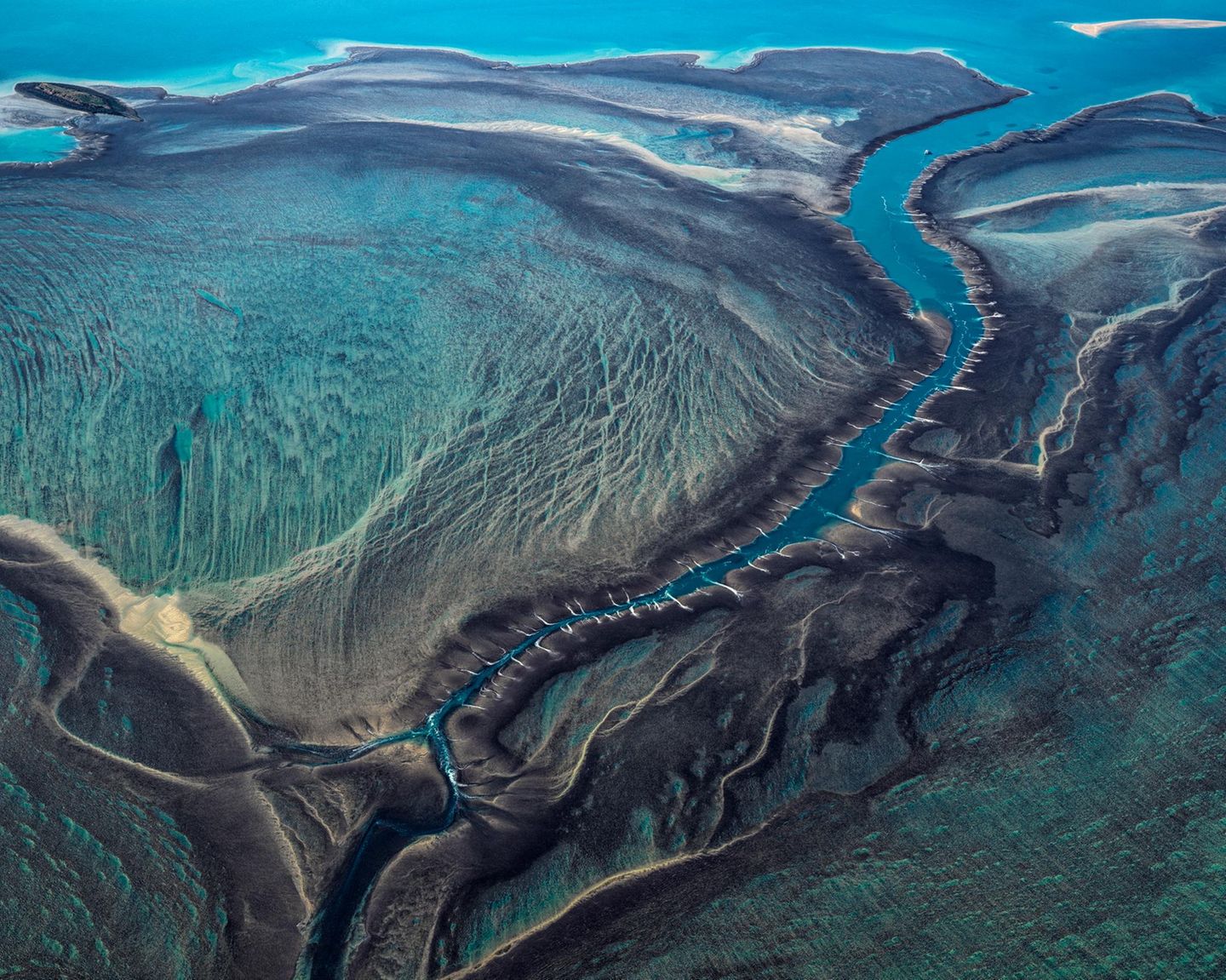 50 Arten Türkis: So leuchtet das Wasser des Montgomery Riff vor der Nordwestküste Australiens. Die Strahlkraft verändert sich je nach Wasserstand, der Tidehub zwischen Niedrigwasser und Hochwasser beträgt hier rund zehn Meter: Bei Ebbe ragt das Riff aus dem Wasser, bei Flut verschwindet es komplett. "Bei Flut liegen Riffplattform und Gezeitenkanal – gleichmäßig überspült– knapp unter dem Meeresspiegel. Bei Ebbe jedoch, wenn der Meeresspiegel innerhalb weniger Stunden tief fällt, fließt das Wasser schneller aus dem großen Gezeitenkanal ab, als es von der Plattform nachfließen kann", schreibt die Geographin Angelika Jung-Hüttl. Dann stürzt es dem Kanal in Wasserfällen über die Riffkante entgegen, die das Riff von oben betrachtet mit Narben übersäen. Der spektakuläre Anblick bleibt den Riffbewohnern verborgen, die sich im vom Gezeitenwechsel bestimmten Lebensraum tummeln: Meeresschildkröten, Wale, Riffhaie, Mantarochen und Salzwasserkrokodile 