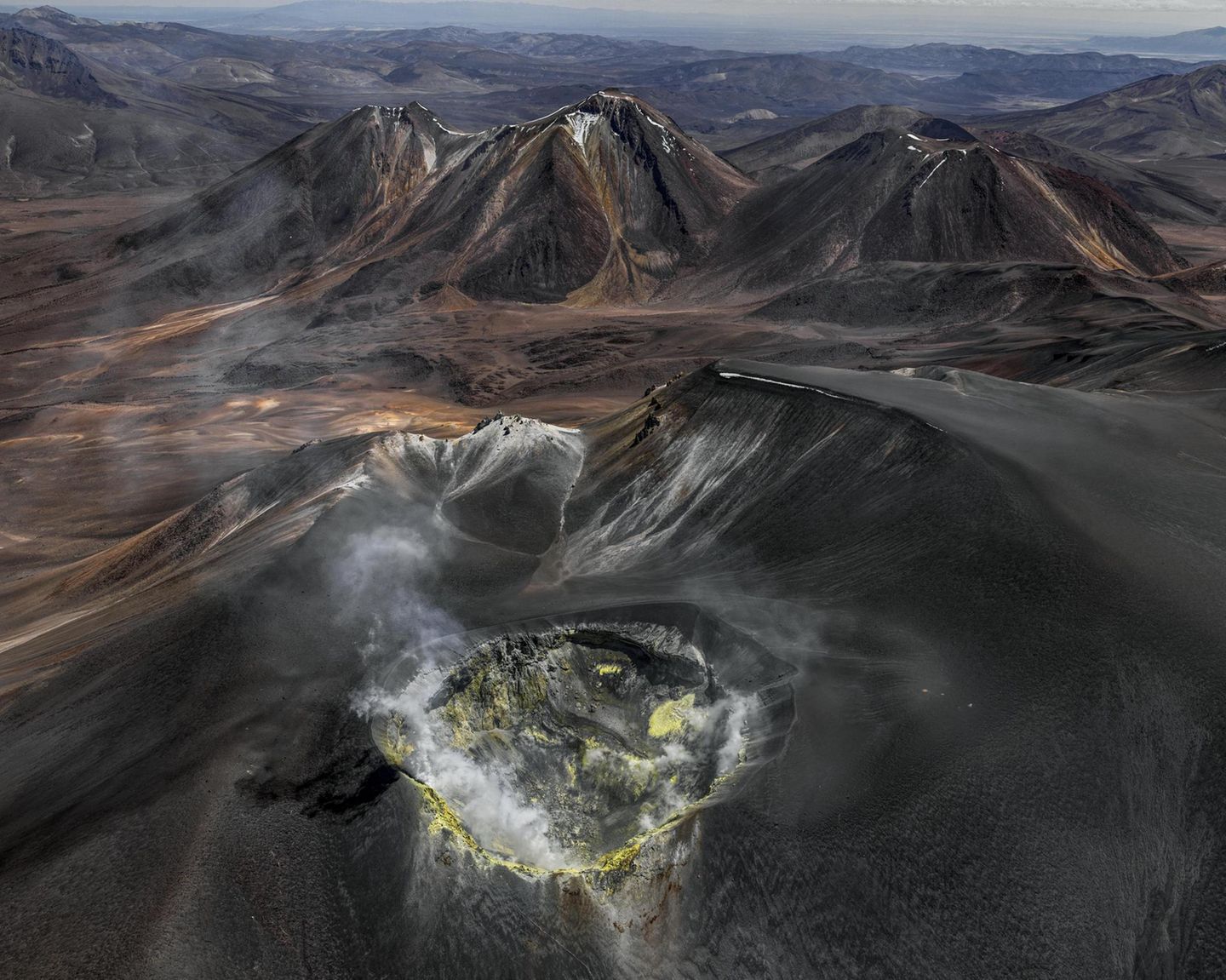 Wie eine eiternde Wunde klafft der Vulkankrater auf dem Gipfel des Isluga, der sich über der kahlen Landschaft des Altiplano an der Grenze zwischen Chile und Bolivien erhebt. Gasschwaden treten aus seinem Inneren; gelb gefärbtes Gestein an den Kraterwänden bezeugt die Schwefelvorkommen, die hier vor einigen Jahrzehnten noch abgebaut wurde. Bernhard Edmaier fotografierte den gewaltigen Krater mit einem Durchmesser von 400 Metern aus der Vogelperspektive und dabei Wissenschaft und Kunst vereint. Der Fotograf und Geologe zeigt mit seinen spektakulären Luftaufnahmen im Bildband "Elements", mit welcher Macht die Natur Landschaften formt – nicht nur hier, in der Hochebene der Anden, sondern auf allen Kontinenten 