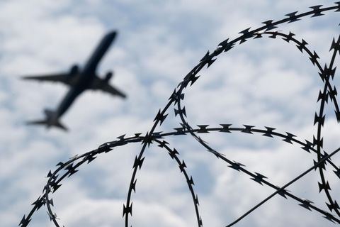 Ein Flugzeug startet hinter einem Zaun mit Natodraht – Symbolbild Abschiebung nach Syrien