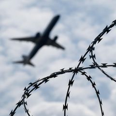 Ein Flugzeug startet hinter einem Zaun mit Natodraht – Symbolbild Abschiebung nach Syrien