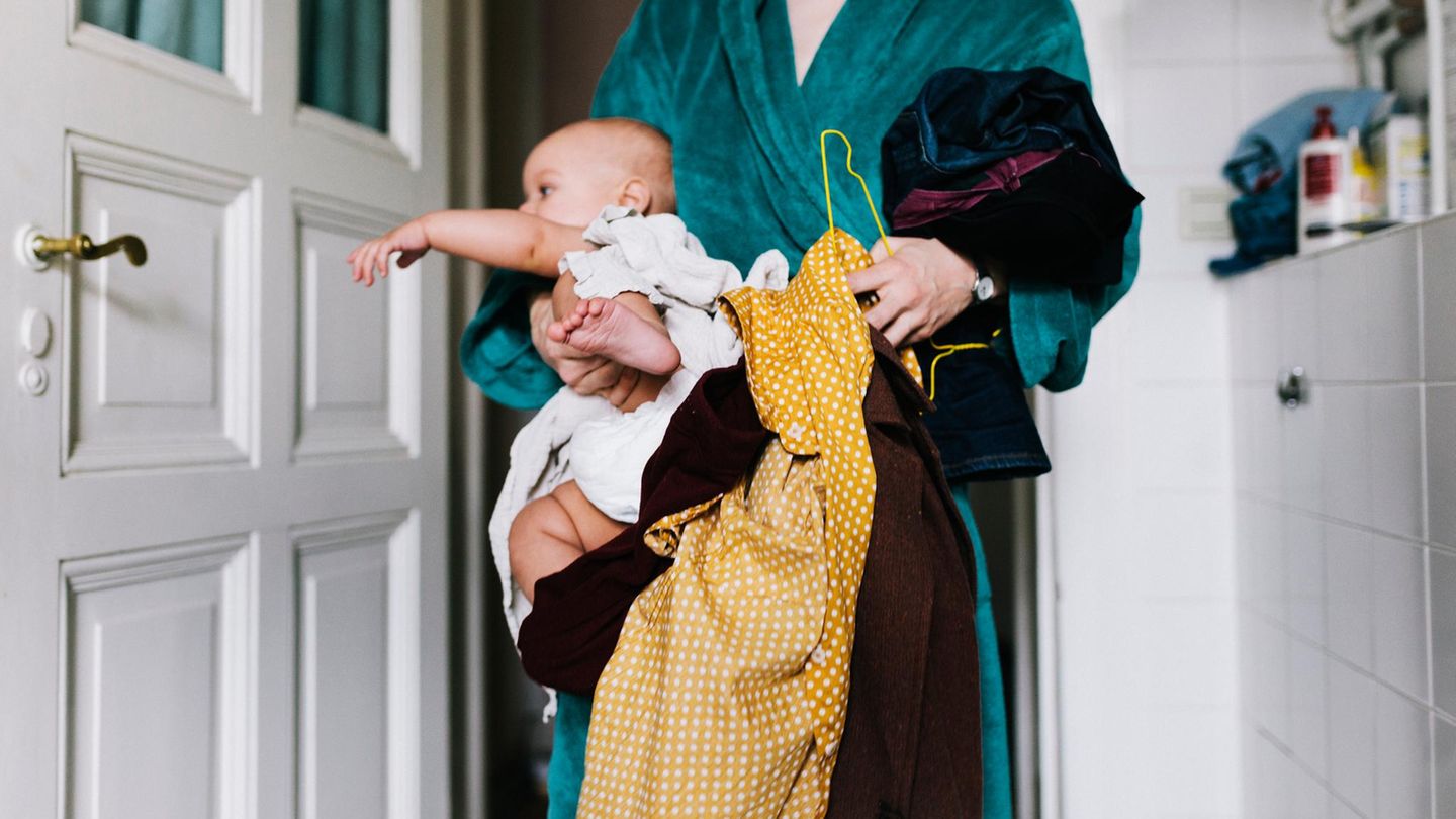 Alleinerziehende Mutter mit Kind und Kleidung auf dem Arm