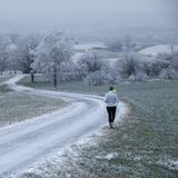 Uttenweiler, Deutschland. Eine Joggerin ist an Heiligabend in der mit Schnee und Raureif bedeckten Landschaft unterwegs. Es ist kalt wie lange nicht an diesem heiligen Tag, und frühmorgens wirkt die Natur fast weiß. Nur richtig viel Schnee fehlt, trotzdem sieht es ein bisschen wie weiße Weihnacht aus