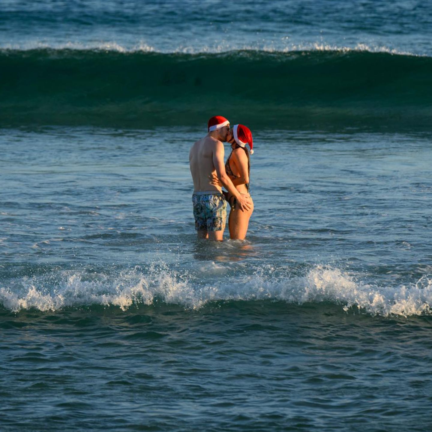 Sydney, Australien. Ein Liebespaar mit Weihnachtsmützen küsst sich in den Fluten am Bondi Beach. Im hochsommerlichen Australien ist es üblich, an Weihnachten und zwischen den Tagen an den Strand zu gehen. Diesmal fällt es allerdings schwerer. Noch immer herrscht Trauer um der Opfer des antisemitischen Terroranschlags, bei dem ein Vater und sein Sohn im Auftrag des IS 15 Juden während der Chanukka-Feier erschossen      
