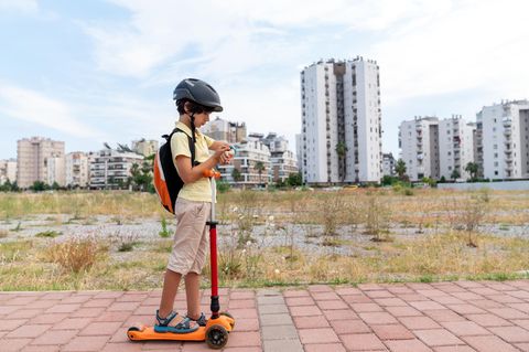 Kinder sind gern draußen unterwegs: Junge mit Roller auf dem Weg zur Schule