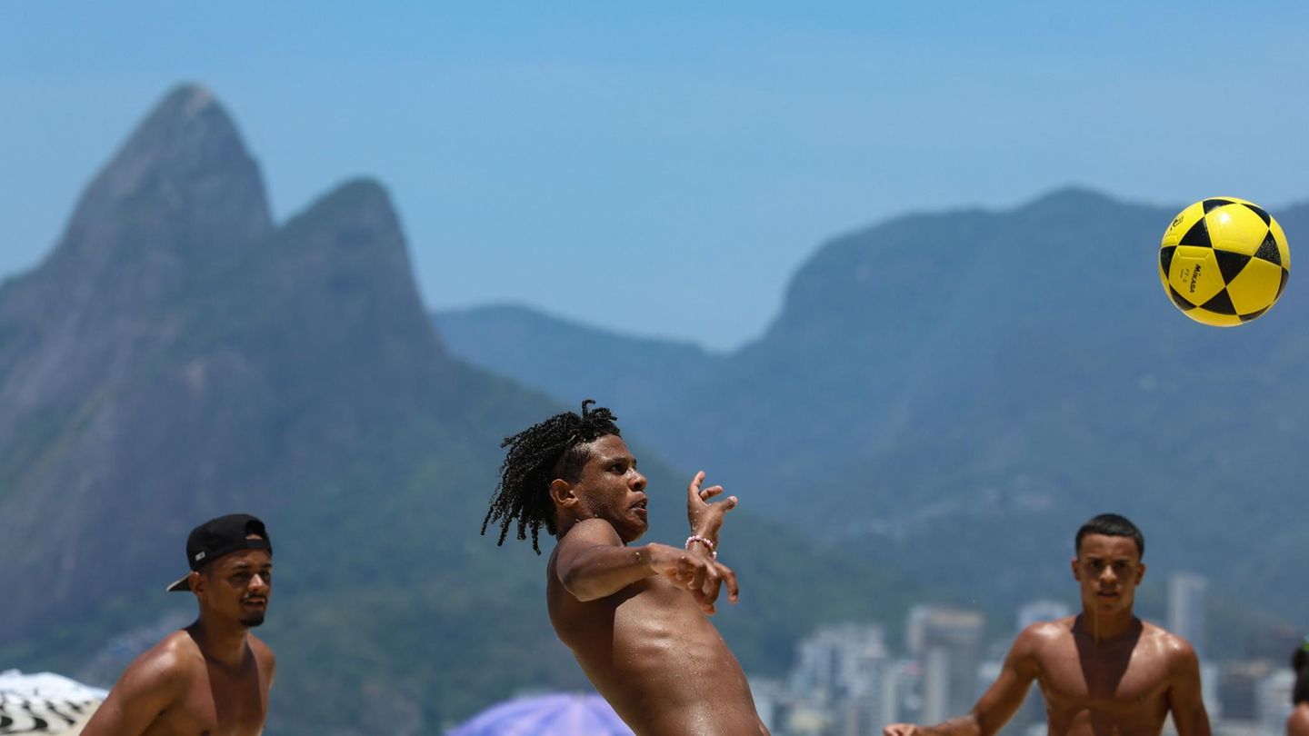 Männer spielen Fußball am Strand, im Hintergrund Rios Hügellandschaft