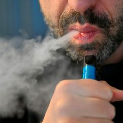 Mann mit E-Zigarette pustet Rauch aus