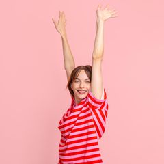 Stress: eine junge Frau mit hochstreckten Armen vor pinkem Hintergrund