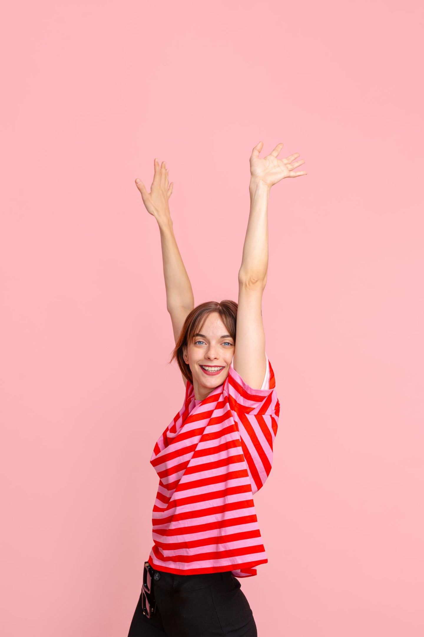 Stress: eine junge Frau mit hochstreckten Armen vor pinkem Hintergrund