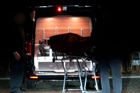 Zwei Männer schieben im Dunkeln eine Bahre mit Leichensack in