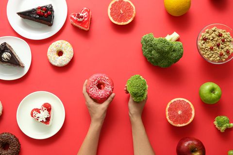 links liegen ungesunde Lebensmittel, rechts gesunde, je eins davon wird in der Hand gehalten