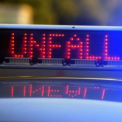 Auf einem Polizeiwagen blinkt Blaulicht neben der roten Leuchtschrift "Unfall"