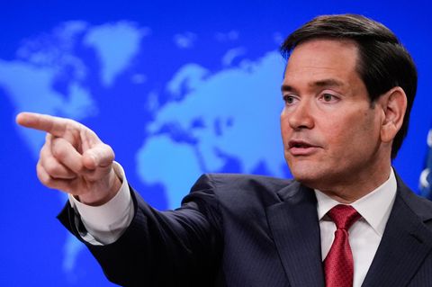 US-Außenminister Marco Rubio sitzt vor einer blauen Weltkarte und zeigt mit seinem rechten Zeigefinger in eine Richtung