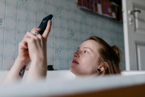 Gasanbieter wechseln: Eine junge Frau liegt in der Badewanne und schaut auf ihr Handy