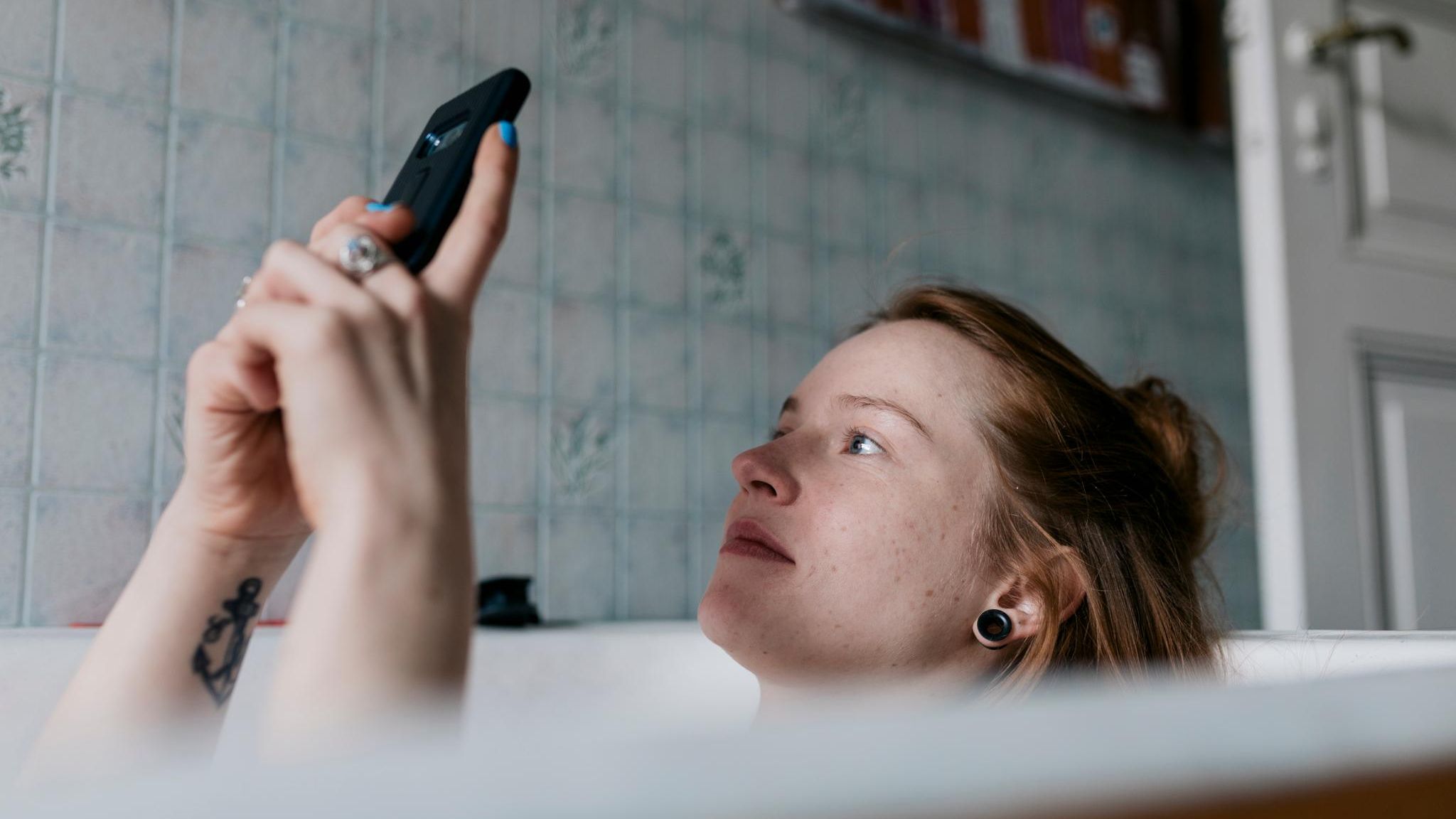 Gasanbieter wechseln: Eine junge Frau liegt in der Badewanne und schaut auf ihr Handy