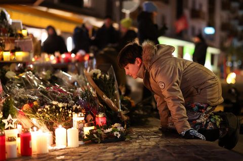 Ein Kind kniet von den Blumen und Kerzen, die Menschen aus Trauer in Crans-Montana abgestellt haben