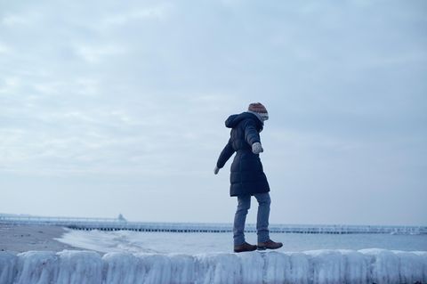 Frau balanciert unsicher auf einer glatten Buhne aus Eis am Meer