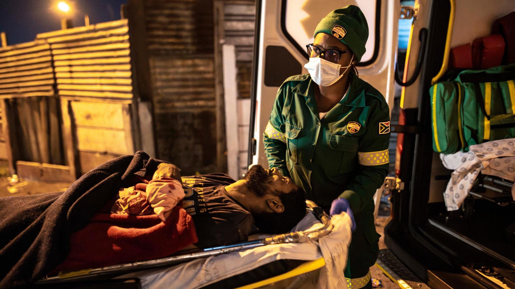 Ein Mann aus Kapstadt wird von einem Rettungssanitäter auf der Liege in den Krankenwagen getragen