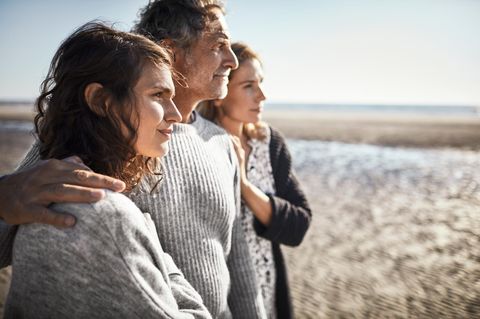 Zwei Frauen und ein Mann stehen eng zusammen am Strand. Was ist ihre Beziehung zueinander?