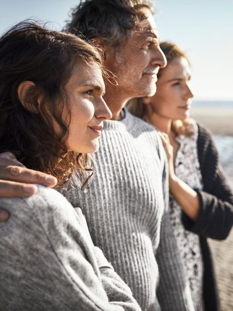 Zwei Frauen und ein Mann stehen eng zusammen am Strand. Was ist ihre Beziehung zueinander?