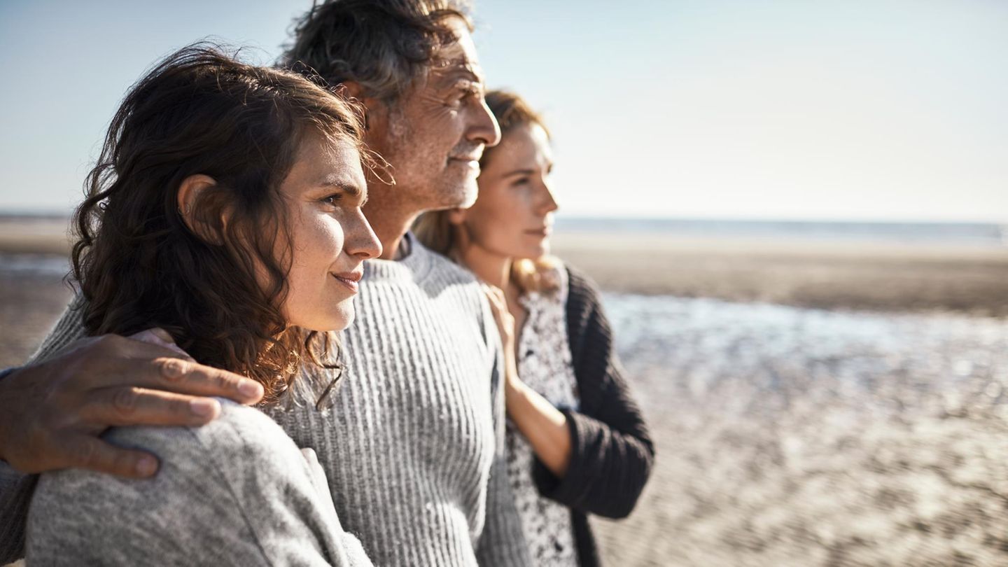 Zwei Frauen und ein Mann stehen eng zusammen am Strand. Was ist ihre Beziehung zueinander?