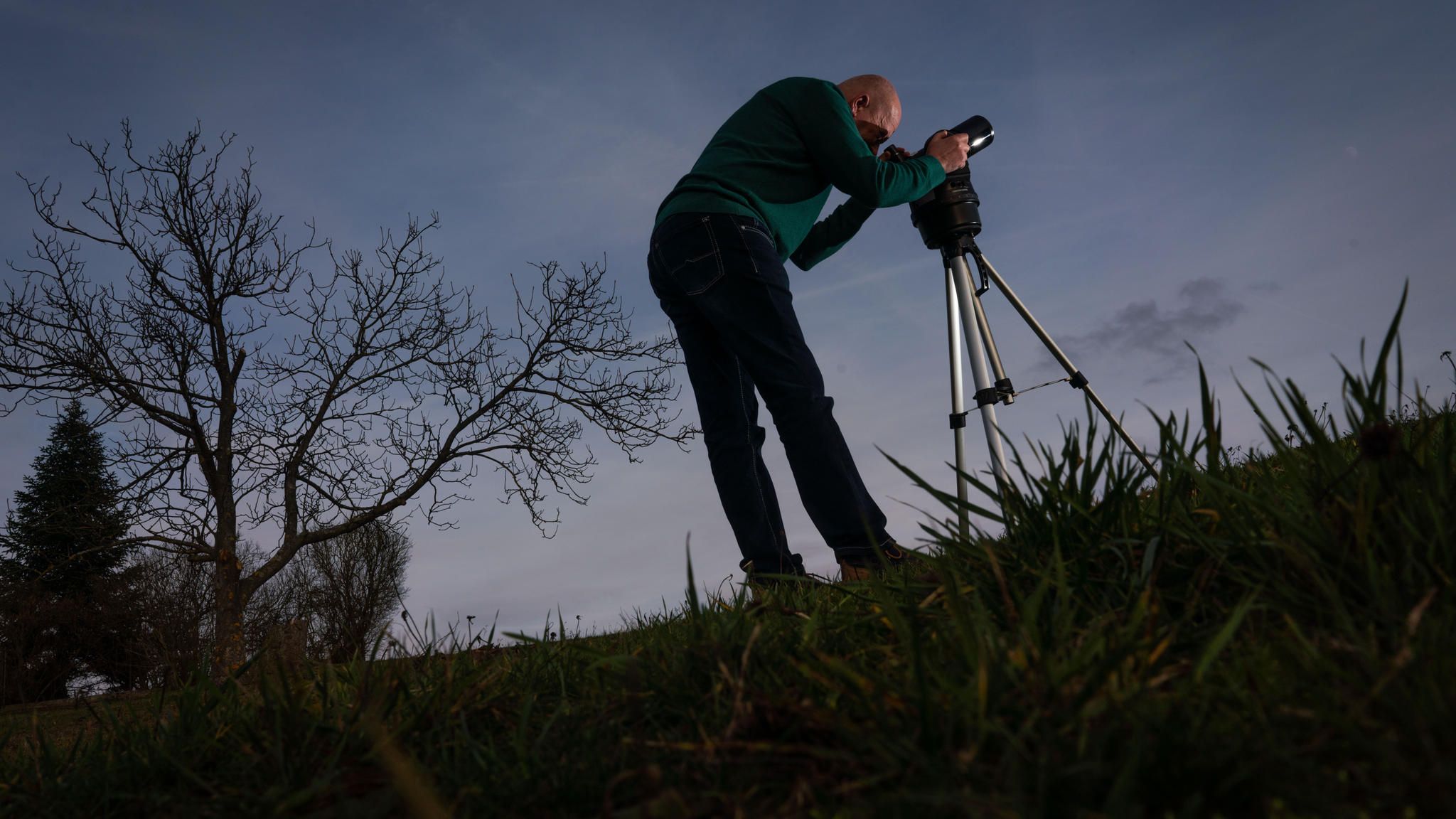 Mann steht mit Teleskop auf einer Wiese