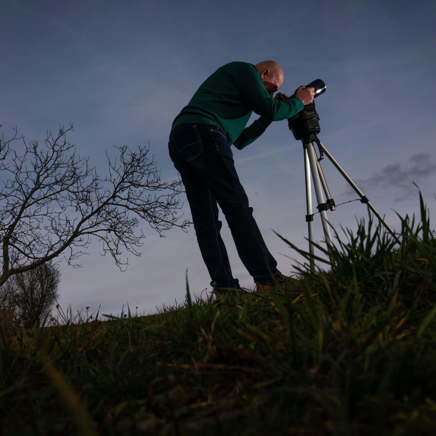 Mann steht mit Teleskop auf einer Wiese