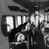 Acht Passagiere liegen auf umgelegten Sitzen in einer Flugzeugkabine, um 1930