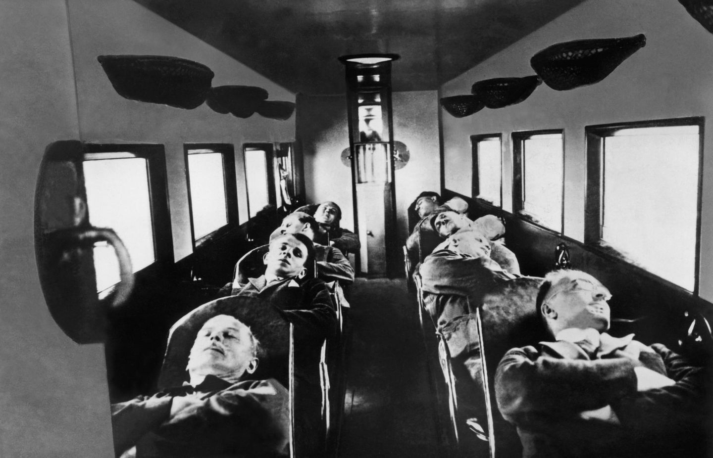 Acht Passagiere liegen auf umgelegten Sitzen in einer Flugzeugkabine, um 1930