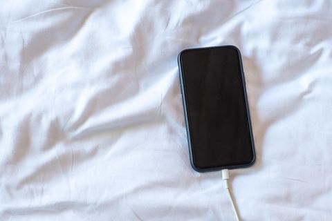 Ein iPhone liegt am Ladekabel im Bett
