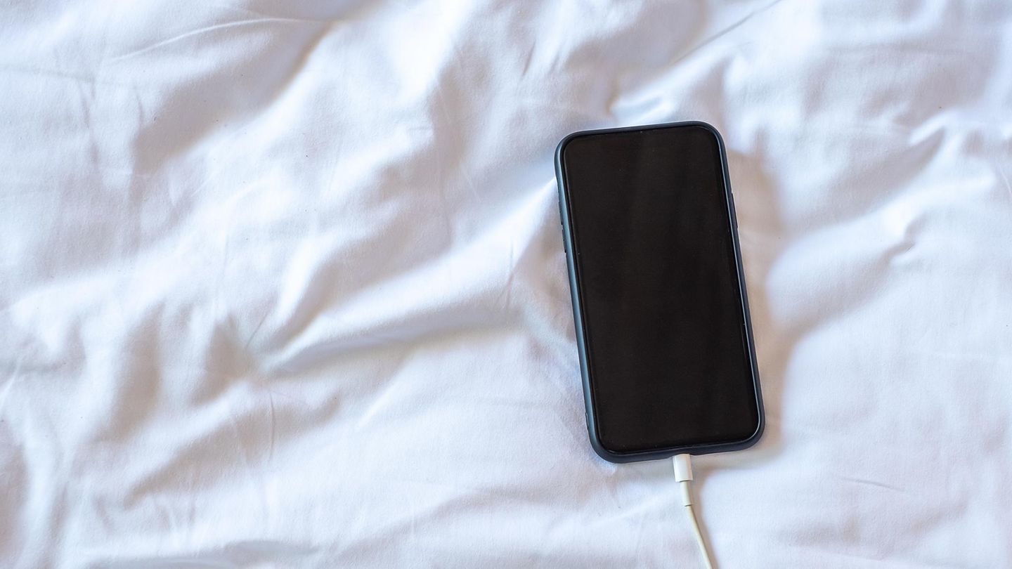 Ein iPhone liegt am Ladekabel im Bett