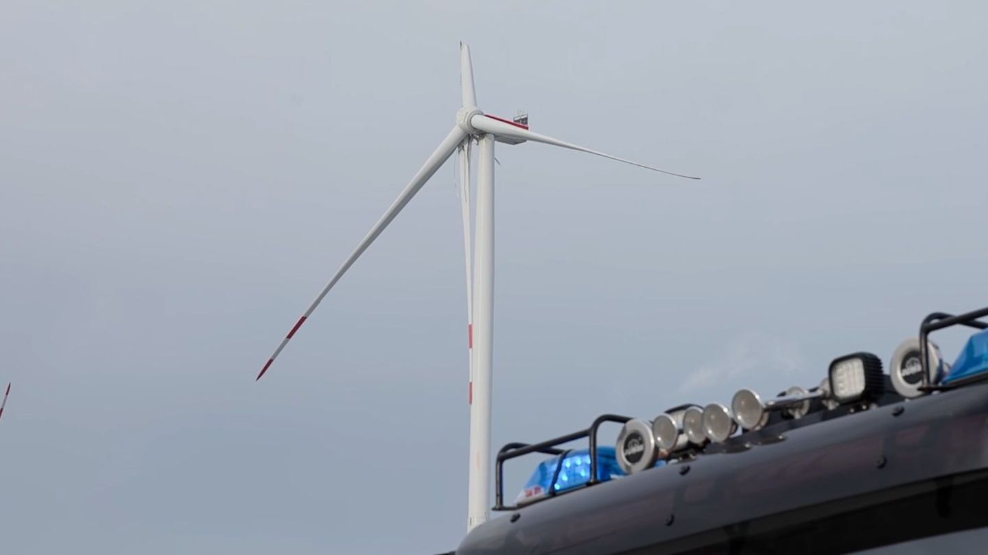 Ein Fahrzeug der Feuerwehr steht vor einem Windrad, bei dem ein Flügel beschädigt ist