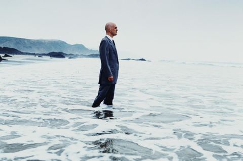 Mann im Anzug steht im Meer und blickt in die Ferne