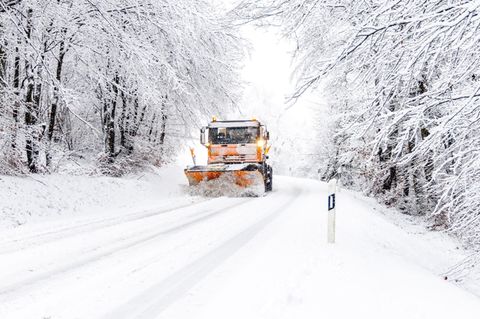 Ein Räumfahrzeug fährt auf einer schneebedeckten Straße und räumt den Asphalt frei