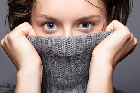Haut im Winter: junge Frau zieht sich grauen Wollpullover übers Kinn