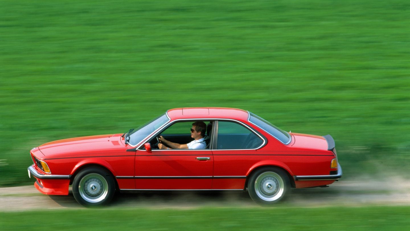 Ein roter BMW Coupé rast über einen Feldweg. Rundherum ist alles leuchtend grün
