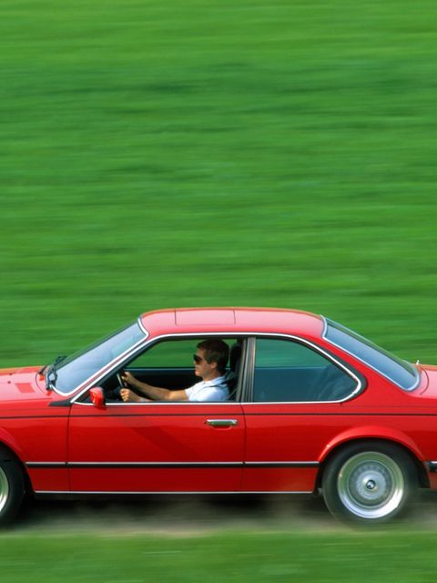 Ein roter BMW Coupé rast über einen Feldweg. Rundherum ist alles leuchtend grün