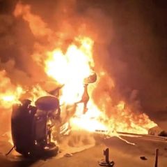 Ein brennenden Auto liegt auf der Seite.